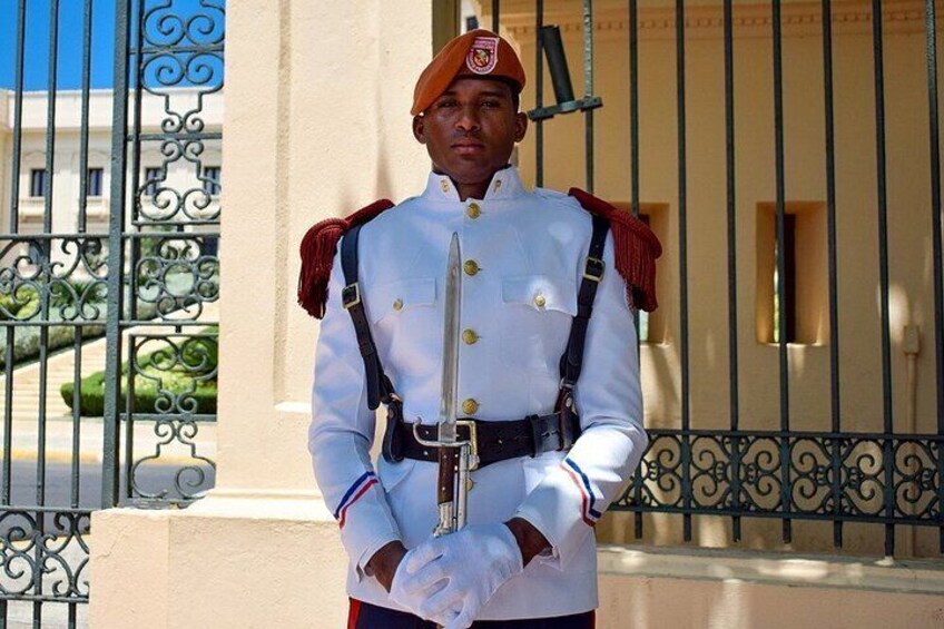 A uniformed guard standing in front of a gate with ornate metalwork. 3