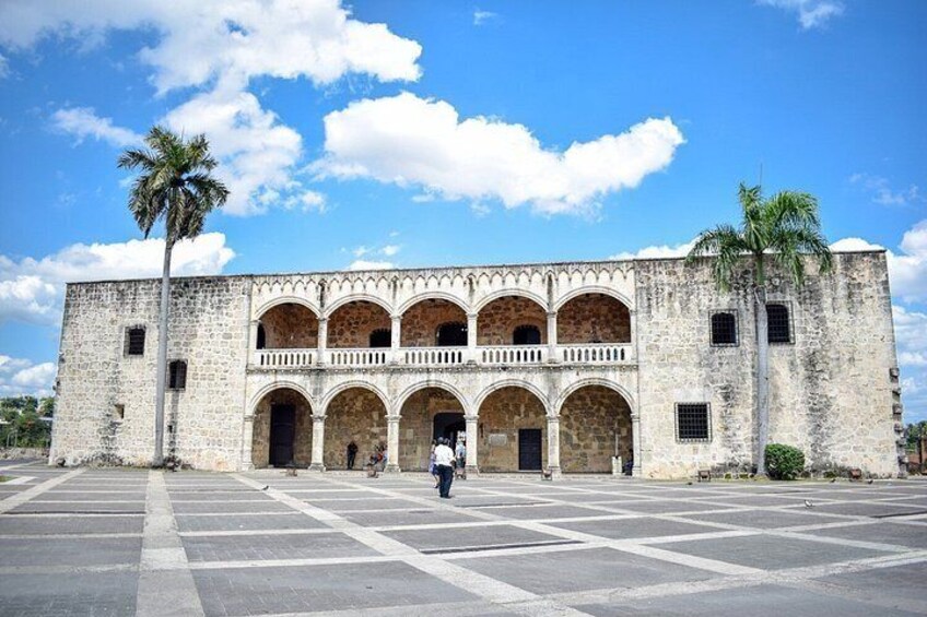 A historic building with multiple arches and a central balcony, surrounded by a paved plaza. 4