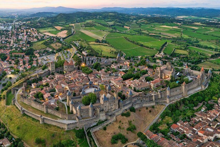 A medieval town with a fortified castle, surrounded by green fields and a river. 2