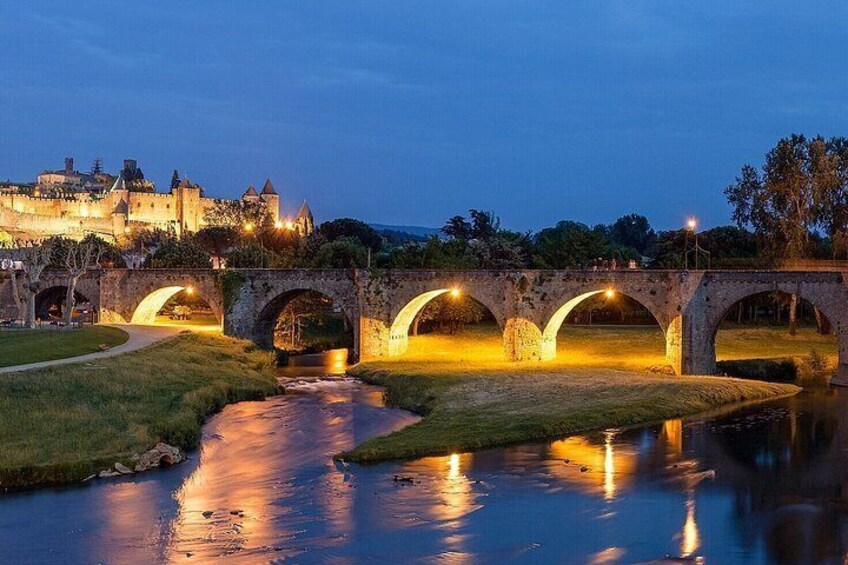 A stone bridge over a river at dusk with castle lights in the background. 4