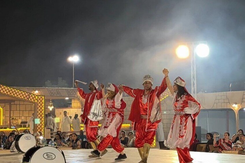 A group of people in red and white costumes performing on a stage with a drum set in the foreground. 4