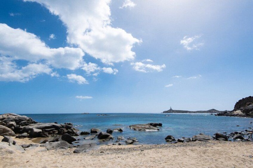A rocky beach with clear blue water, a distant lighthouse, and a partly cloudy sky. 3