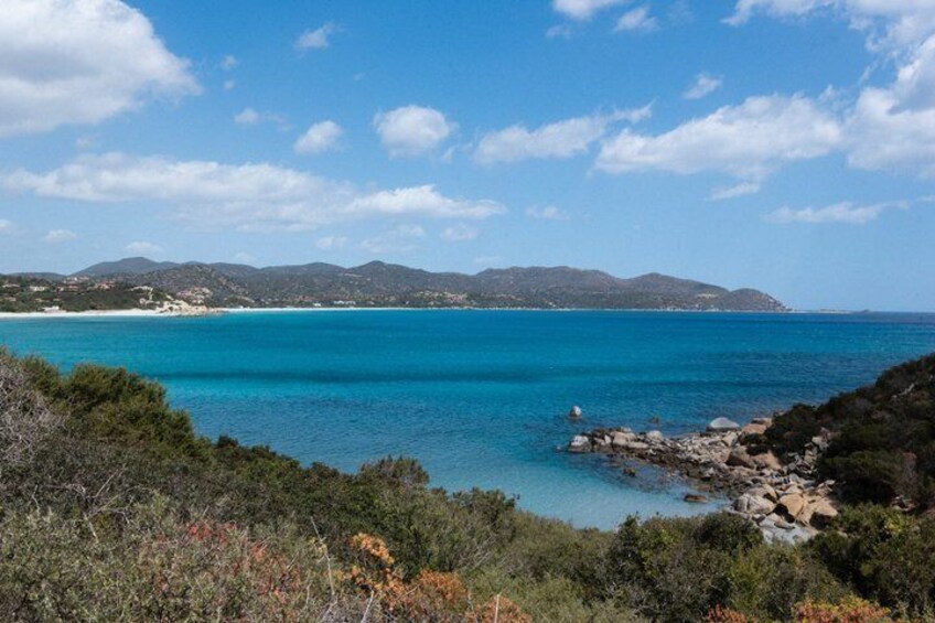 A coastal landscape with clear blue waters, rocky shorelines, and distant mountains under a partly cloudy sky. 2