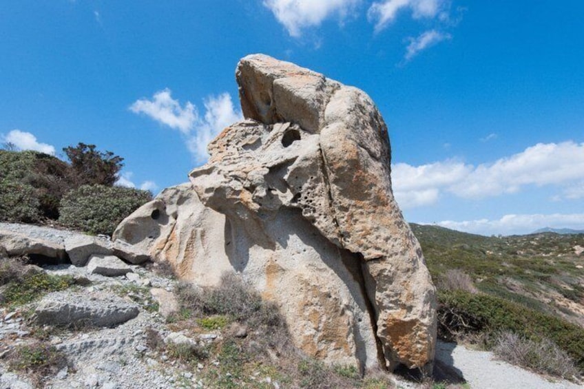 A large rock formation with a prominent overhang, surrounded by sparse vegetation and a clear blue sky. 5