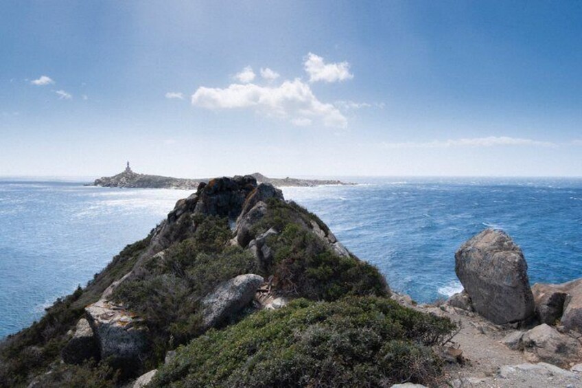 A coastal landscape with rocky terrain, a lighthouse, and the ocean. 1