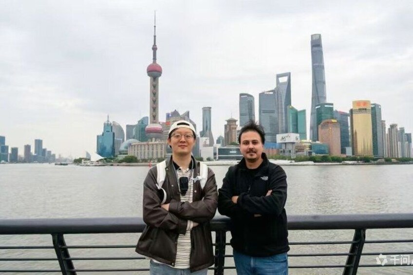 Two people standing by a river with a city skyline in the background. 3