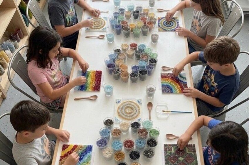 Children engaged in a craft activity, creating colorful patterns with beads on a table. 2