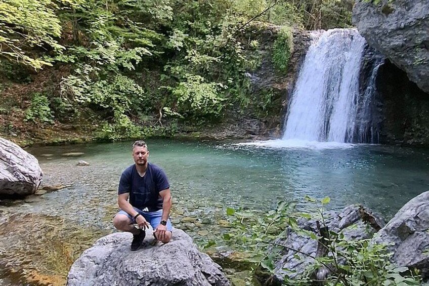 A waterfall, a person sitting on a rock, and a river. 1