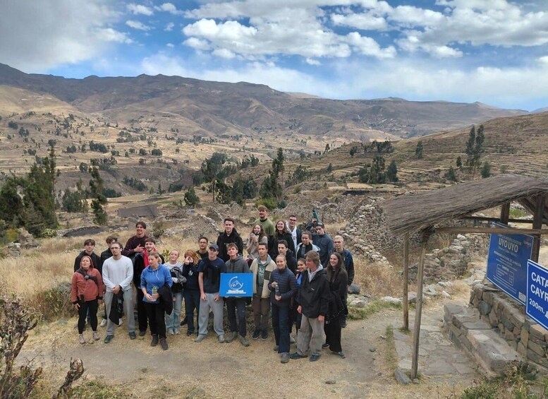 Un grupo de personas en un paisaje rural, con montañas al fondo y un cartel que indica la distancia a Cayro. 2