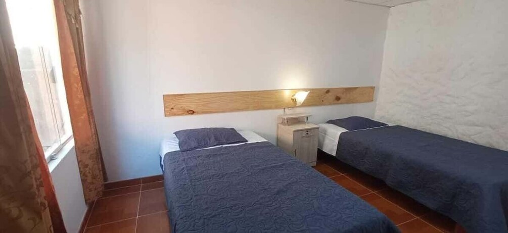 Un dormitorio con dos camas, cabecera de madera, mesita de noche y ventana con cortinas. 4