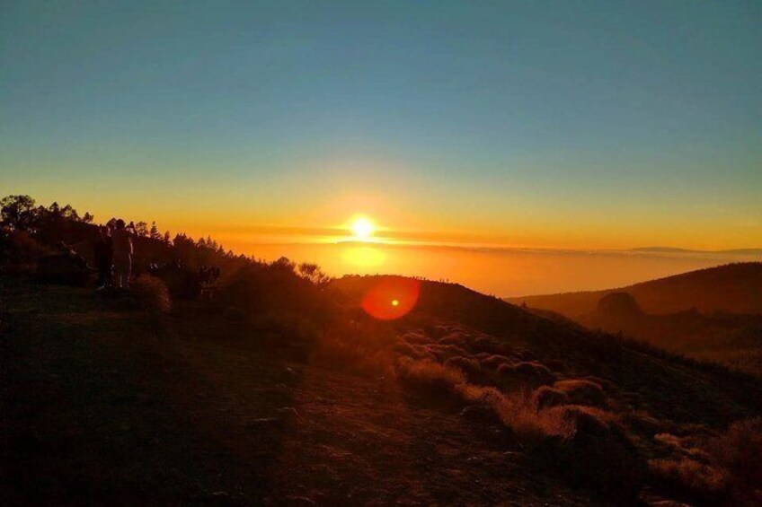 A sunset over a hilly landscape with a path leading towards the sun. 2