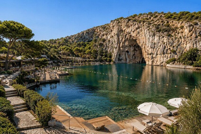 A clear blue lake with a rocky cliff, a wooden deck, and outdoor seating. 1