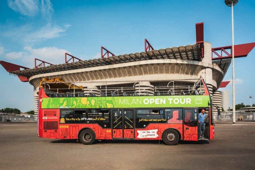 Un autobus a due piani rosso con la scritta 'Milan Open Tour', parcheggiato di fronte a uno stadio. 3