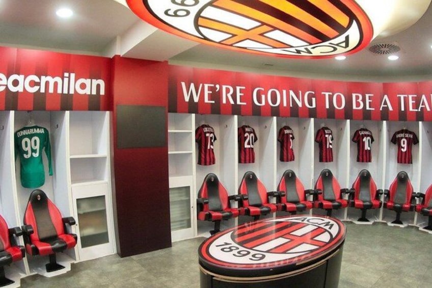 Spogliatoio sportivo con pareti a righe rosse e nere, divise da squadra rossa e nera appese e un emblema circolare sulla parete. 2