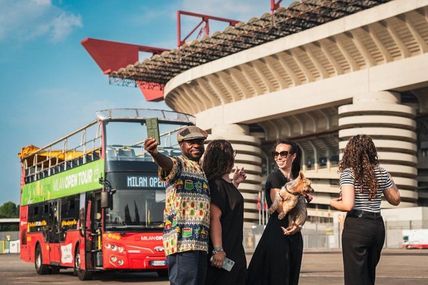 A group of people standing in front of a bus and a stadium. 5