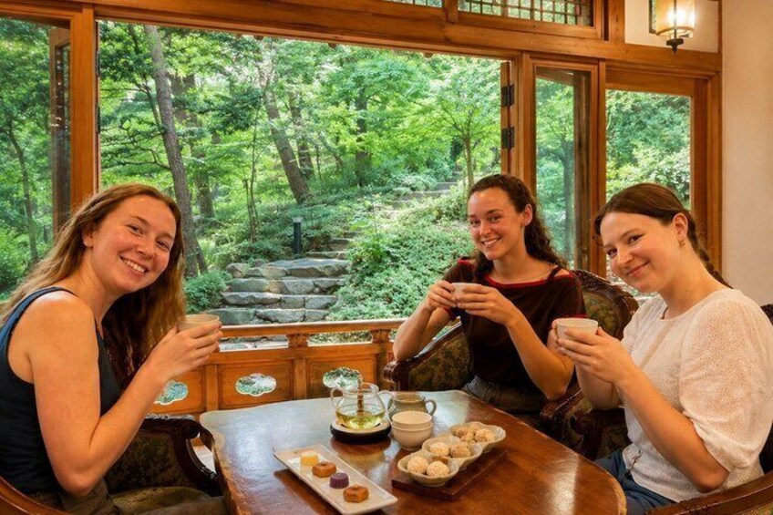 Three people sitting at a table with a view of a forested area through large windows. 1