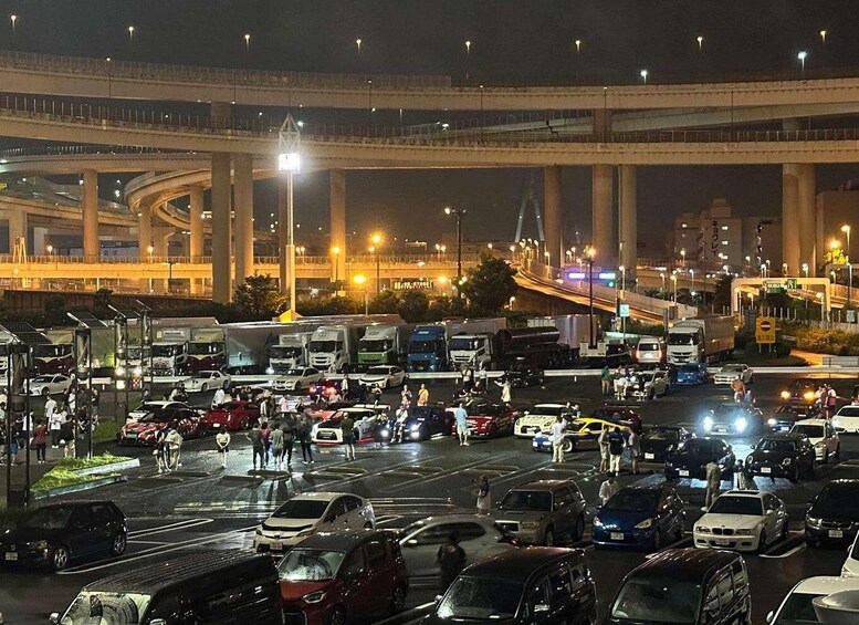 A busy urban intersection with multiple lanes of traffic and a large overpass in the background. 3