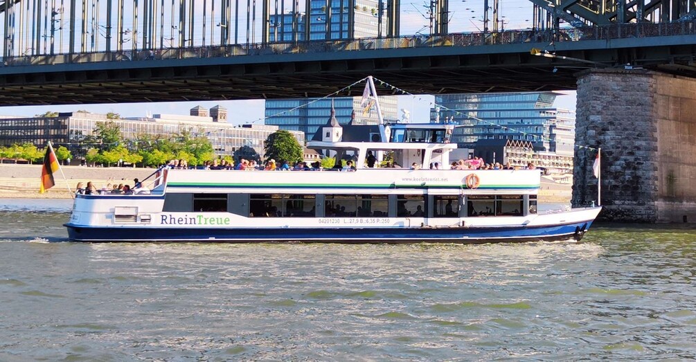 A river cruise boat named RheinTreue with passengers, passing under a bridge. 5