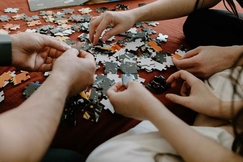 A group of people assembling a jigsaw puzzle on a red surface. 2
