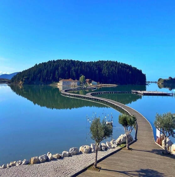 A calm lake with a wooden walkway curving around a small island, surrounded by trees and rocks. 1