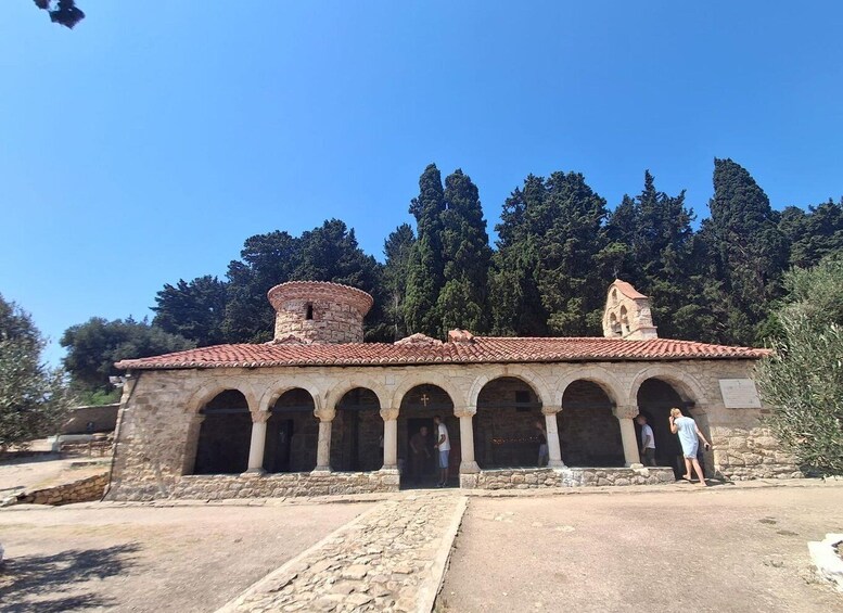 A stone building with a tiled roof, arched doorways, and a bell tower. 5