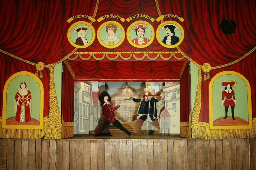 A theater stage with red curtains, a central figure in a red outfit, and four framed portraits above. 1