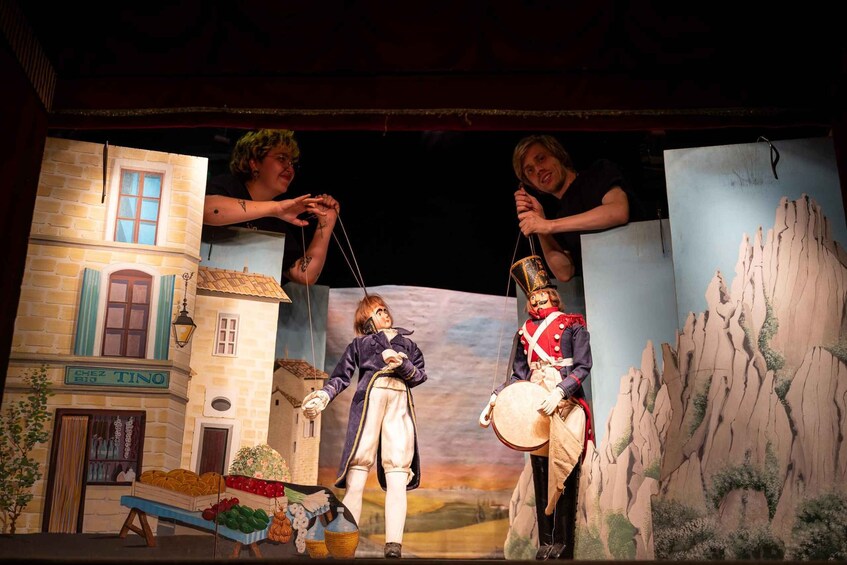 A puppet theater with a puppet playing a drum, another puppet holding a string, and a third puppet in a building. 2