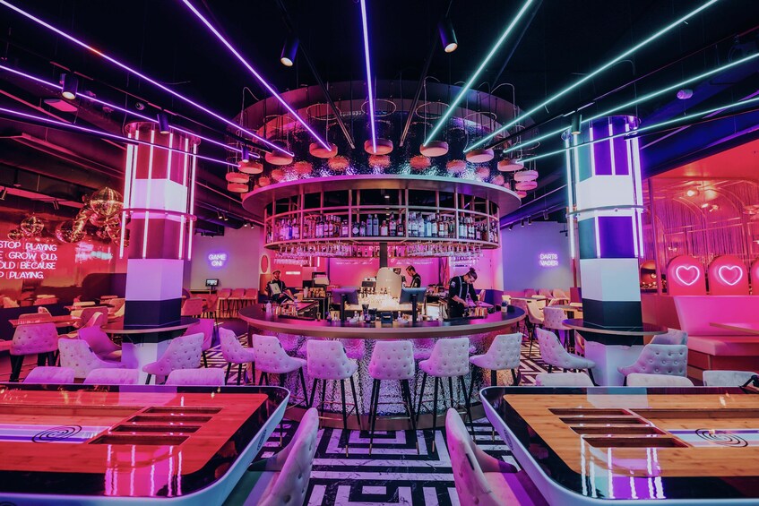 A bar with a circular layout, neon lights, and a variety of seating options. 2