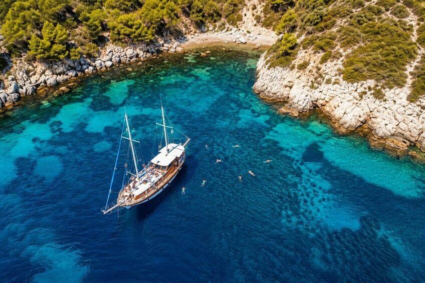 A sailboat anchored in clear blue waters near a rocky coastline with sparse vegetation. 3