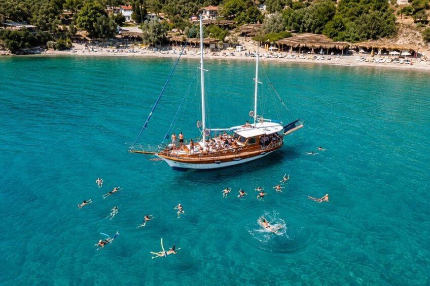 A boat with people on it, surrounded by clear blue water and a beach with people swimming. 4