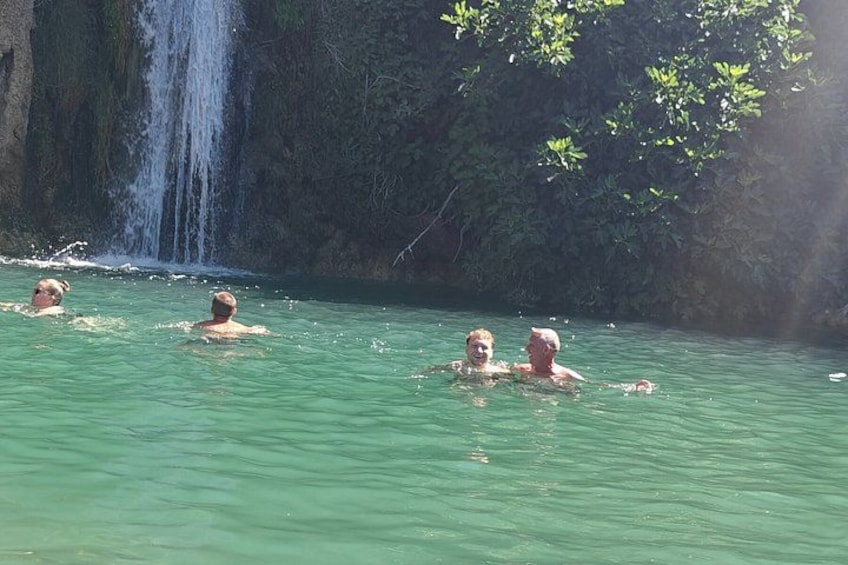 A waterfall, clear water, and people swimming. 2
