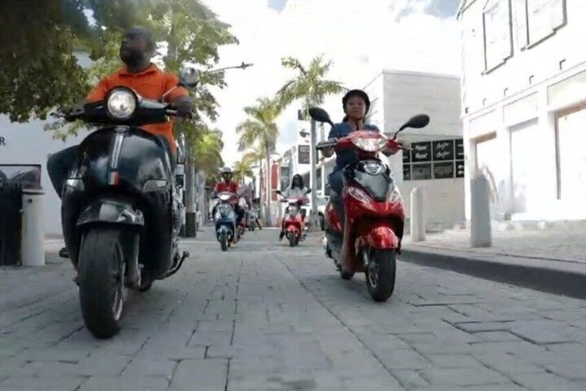 A street with multiple scooters, buildings, and palm trees. 4