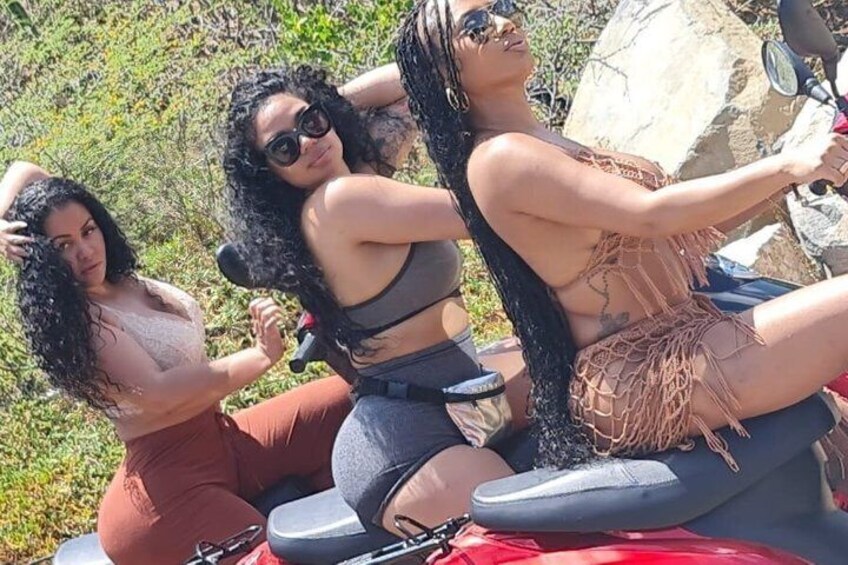 Three people on a motorcycle, one in a white top and red pants, another in a black top and blue pants, and the third in a brown top and blue pants. 3