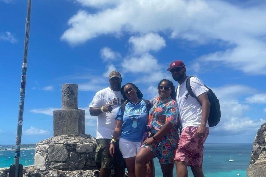 A group of people standing on a rocky outcrop with a clear view of the ocean and a stone structure in the background. 2