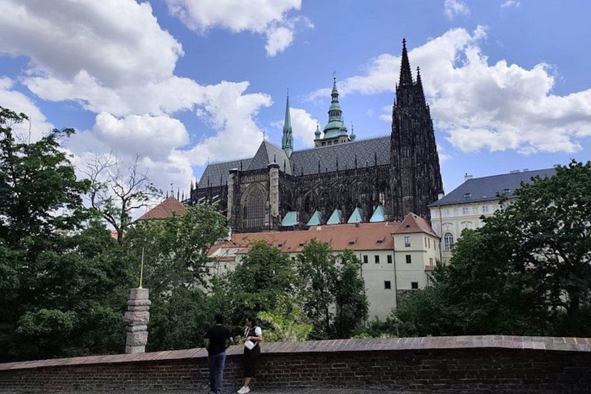 A historic cathedral with a tall spire and a clock tower, surrounded by trees and a brick wall. 1