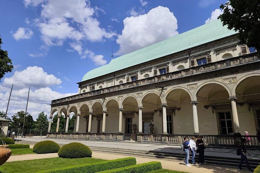 A classical building with a green roof, arched colonnades, and a paved courtyard. 3