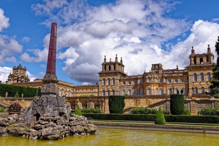 A historic building with a tall obelisk, a fountain, and well-manicured gardens. 4