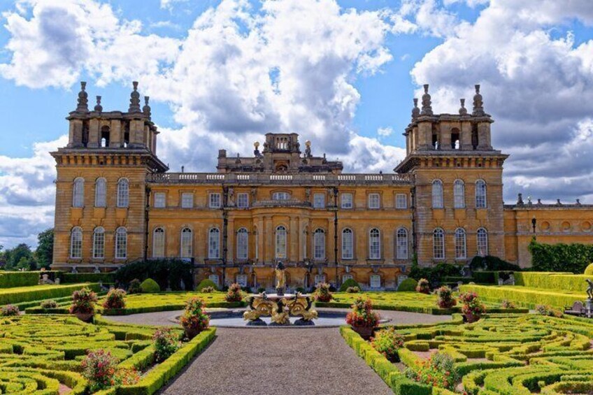 A grand historic building with symmetrical architecture, manicured gardens, and a central fountain. 1