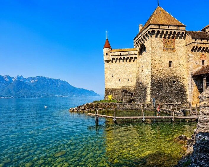 A historic castle by a clear lake with mountains in the background. 5