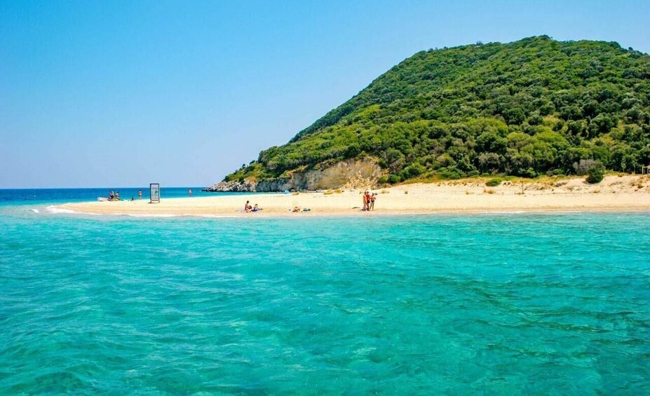 A beach with clear turquoise water, sandy shore, and a hill with dense greenery in the background. 3