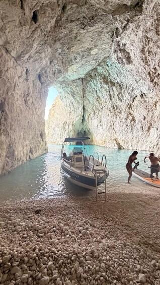 A boat docked in a rocky cave with two people paddleboarding nearby. 4