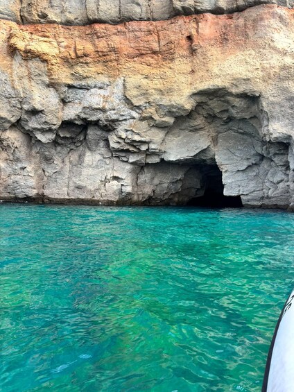 A rocky cliff with a cave entrance and clear turquoise water. 5