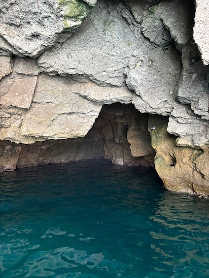 A rocky cave entrance with clear blue water below. 4