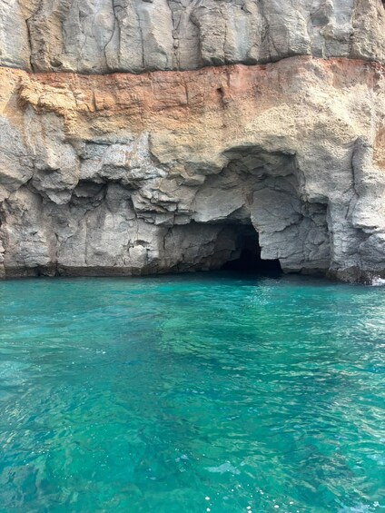 A rocky cliff with a cave entrance and clear turquoise water. 3
