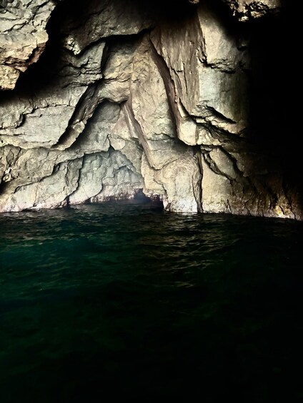 A cave with stalactites and stalagmites, water at the bottom, and a view into the cave. 5