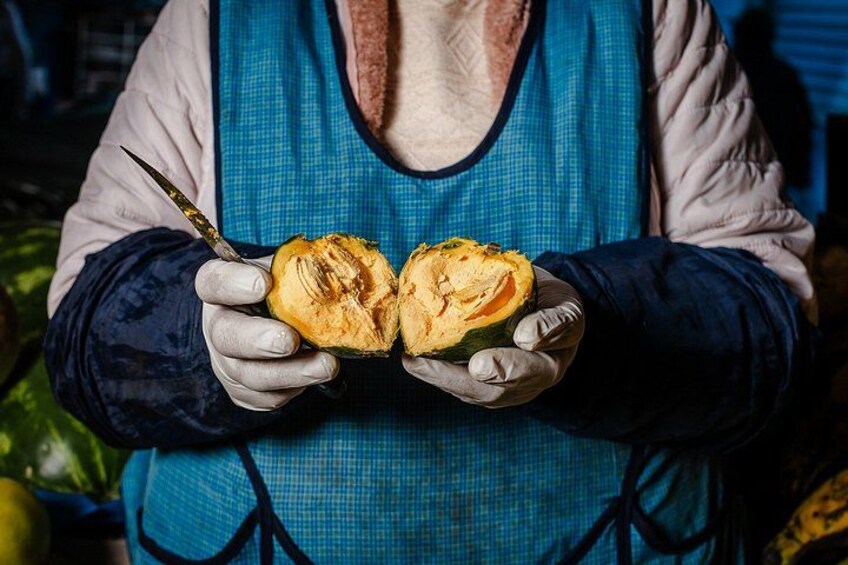 A person holding a halved fruit, wearing gloves, and a blue apron. 2