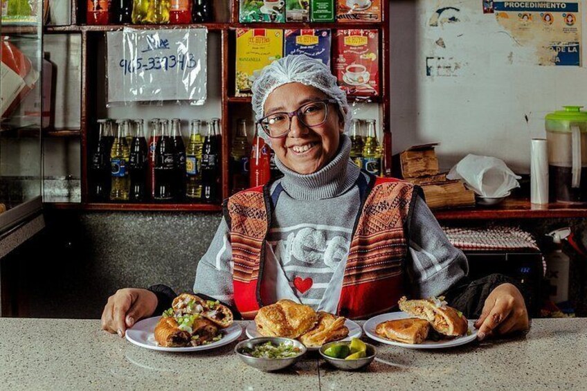 A person sitting at a counter with plates of food, a shelf with bottles, and a sign with text. 4