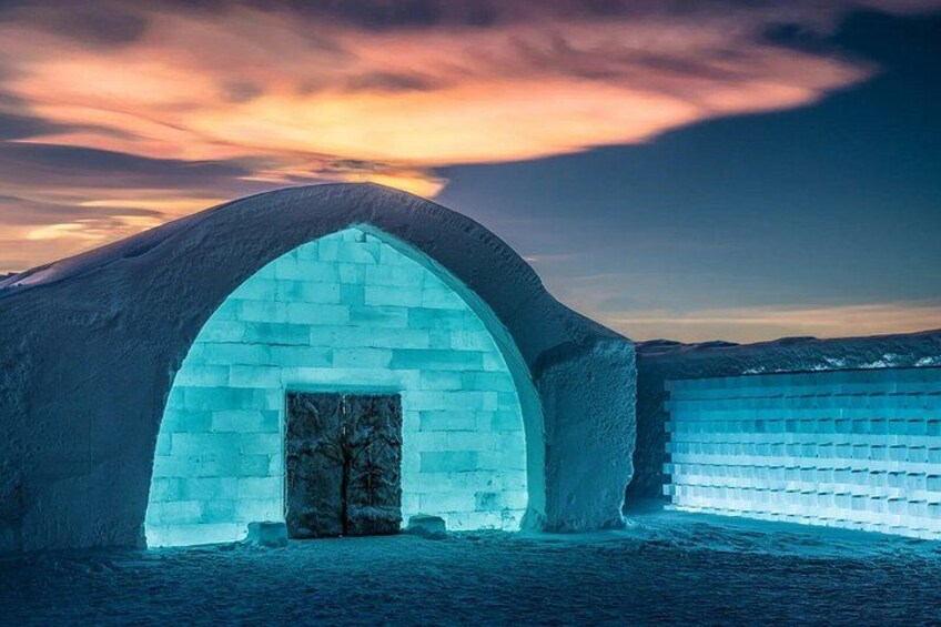 An igloo with a snow-covered entrance and a sunset in the background. 2