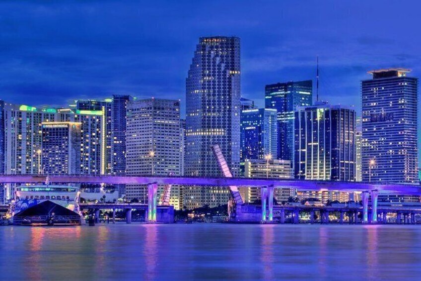 A city skyline at night with illuminated buildings and a bridge over water. 2