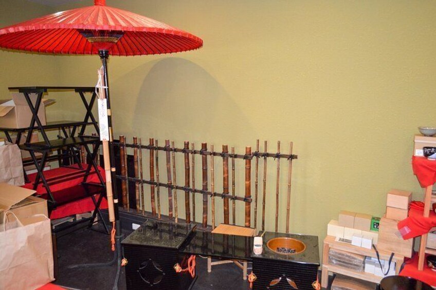 A room with a red umbrella, bamboo sticks, a black table, and various boxes. 5